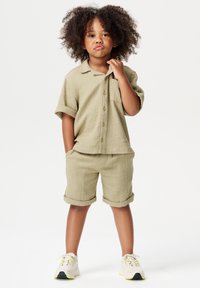 Lichtkhaki twee-delige outfit voor kinderen, met een kortärmige overhemd met knopen en bijpassende shorts, beide gemaakt van een gestructureerde stof.