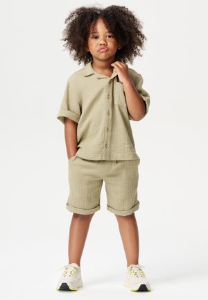 Lichtkhaki twee-delige outfit voor kinderen, met een kortärmige overhemd met knopen en bijpassende shorts, beide gemaakt van een gestructureerde stof.