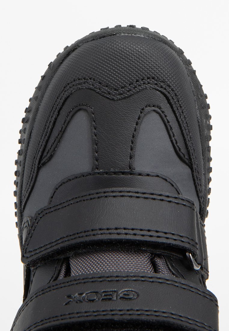 Schwarzer Sportschuh mit Klettverschluss, aus Leder und synthetischen Materialien gefertigt. Texturierte Zehenkappe und gemusterte Sohle sorgen für Traktion.