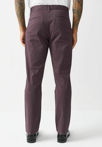 Bordeauxfarbene Hose mit geradem Schnitt, aus glattem Stoff gefertigt. Verfügt über zwei Gesäßtaschen und sitzt auf der Taille, kombiniert mit schwarzen Schuhen.