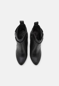 Botas de tobillo de cuero negro con punta afilada, cremalleras laterales y forro de tela. Presentan una textura suave y una lengüeta para facilitar su uso.