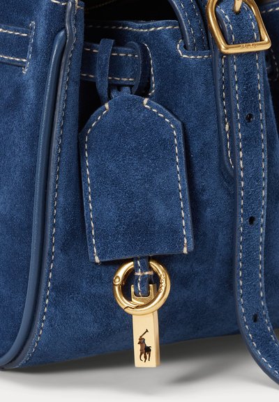 Blå læderhandbag med guld hardware, et lædermærke, kontrasterende syninger og en dekorativ charme med logo detalje.