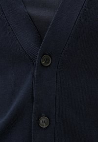 Mörkblå cardigan med V-ringning, med texturerade stickade mönster och en svart tvåhåls knappstängning.