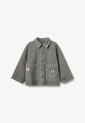 Veste gris boutonnée avec manches larges, deux poches avant, un petit écusson sur la poche gauche et un visage souriant avec texte sur la poche droite.