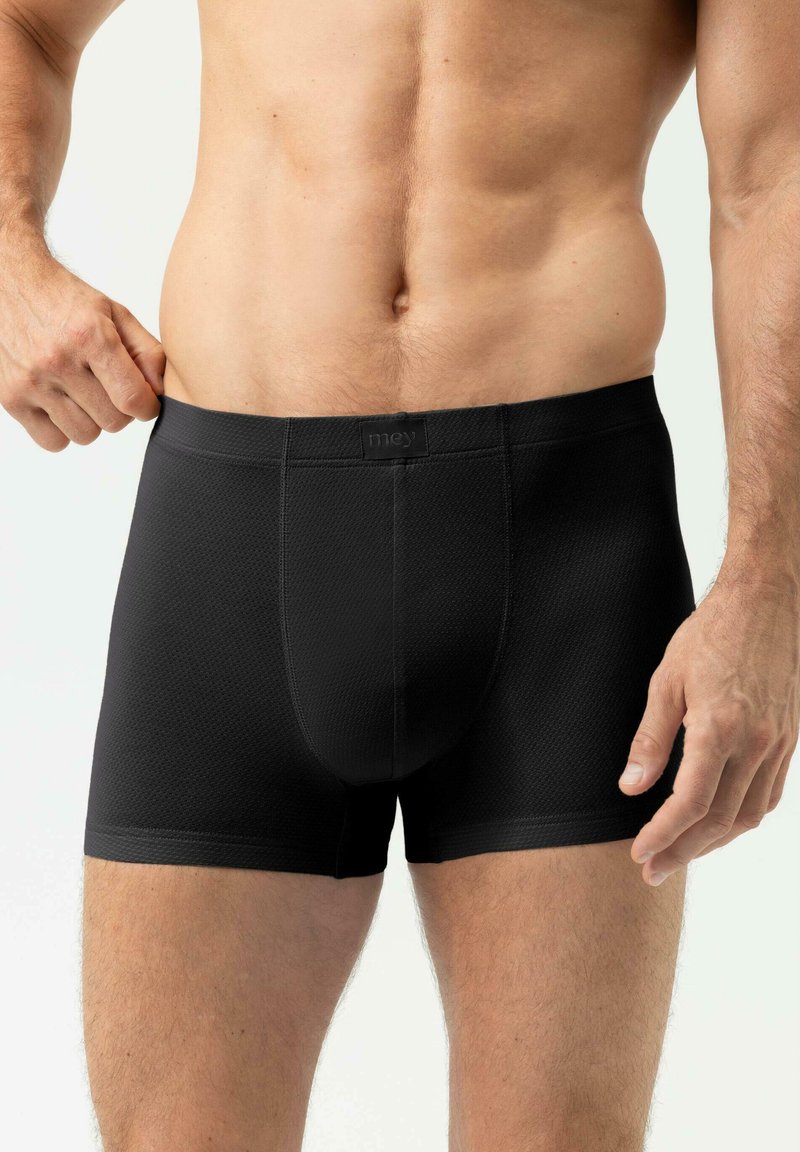 Boxer noir avec un tissu texturé, une ceinture avec logo et une coupe ajustée. Le vêtement présente des jambes courtes et un design avec pochette avant.