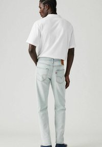 Light blue denim jeans with a straight fit, featuring two back pockets and a brown leather patch at the waistband. White t-shirt is plain.