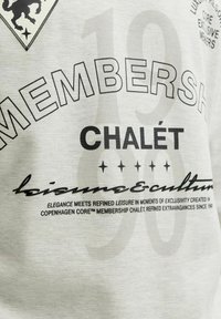 Biely textil s čiernym textom obsahujúcim "MEMBERSH", "CHALET", päť hviezdičiek a menší text o vyberanej rekreácii a exkluzivite.
