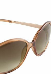 Lunettes de soleil surdimensionnées avec une monture transparente marron et des verres dégradés marron. Elles présentent des branches fines avec un accent argenté gravé "Fabriqué en Chine."