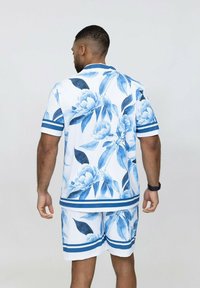 Chemise à manches courtes à fleurs et shorts assortis en blanc avec des motifs de fleurs bleues et des motifs de feuilles, comportant des accents à rayures bleues.