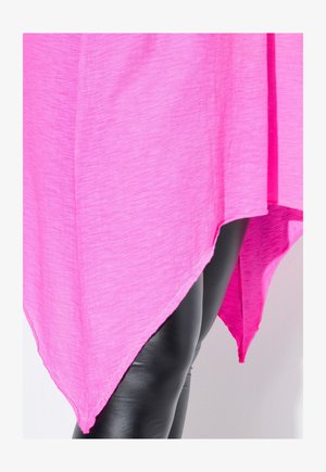 Jasnoróżowy asymetryczny top wykonany z lekkiej tkaniny, z wydłużonym dołem i warstwowym wzorem, zestawiony z czarnymi, błyszczącymi legginsami.