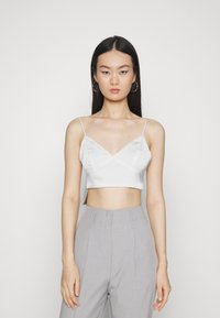 Top cropped de cetim branco com alças finas ajustáveis e design em V, combinado com calças cinza claro de cintura alta, apresentando uma textura suave.