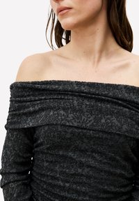 Haut noir épaules dénudées avec un motif floral texturé ; présente des détails froncés et un tissu doux et extensible.