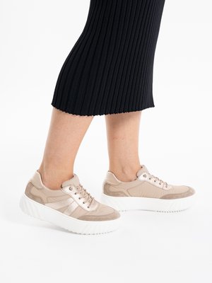 Legs wearing a black ribbed skirt and beige lace-up sneakers with white chunky soles on a white background.