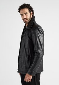 Schwarze Lederjacke mit Reißverschluss, hohem Kragen und einer strukturierten braunen Futterung, seitlichen Reißverschlusstaschen und einer glatten Oberfläche.