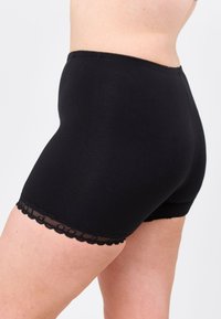Mustat puuvillashortsit, joissa on pitsireunus helmassa. Istuva malli, keskipituiset, joissa on sileä pinta ja yksinkertainen siluetti.