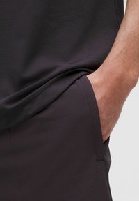 Tummanharmaa urheilupaita, jossa on teksturoitu kangas ja lyhyet hihat, yhdistettynä yhteensopiviin housuihin, joissa on sivutasku ja sileä pinta.