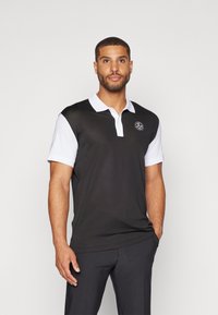 Čierna polo košeľa s bielym golierom a manžetami, so malým logom na hrudi. Hladká látka a priliehavý strih.