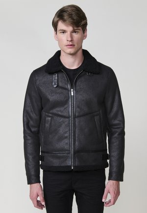 Chaqueta de piel sintética negra con un acabado texturizado, cuello de borreguito, cierre de cremallera y bolsillos laterales. Ajuste slim con un diseño corto.