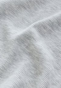 Primer plano de tela suave, gris claro, con finas rayas verticales y pliegues suaves que crean una superficie texturizada y acanalada.