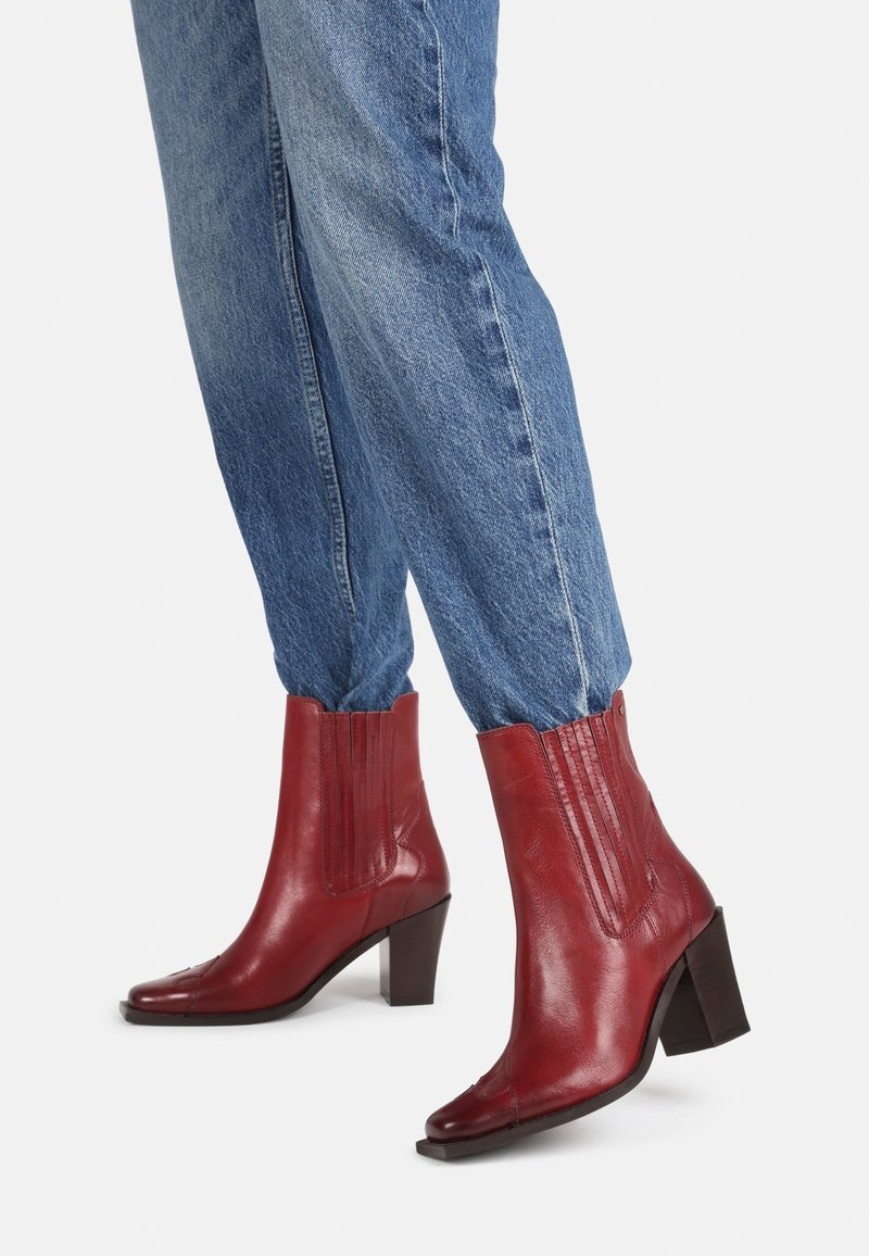 Røde læder ankelstøvler med firkantet tå, ribbede sideaccenter, en mellemhøj blokhæl, parret med blå denimjeans.