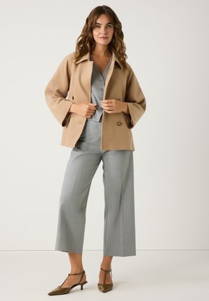 Beige dubbelzijdig jasje met brede mouwen, gecombineerd met een lichtgrijze V-hals top en grijze wijde broek. Bruine puntige hakken.