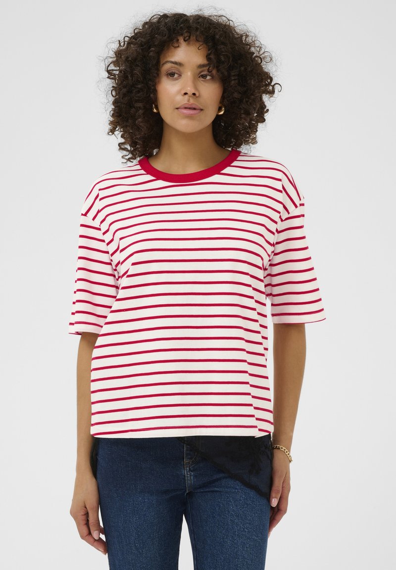 T-shirt à rayures rouges et blanches avec un col côtelé. Manches courtes et coupe ample. Associé à un jean bleu foncé, présentant un ourlet asymétrique.