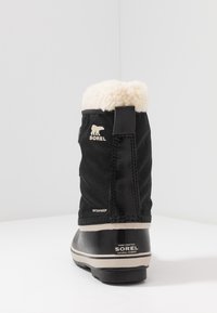 Czarne wodoodporne buty z miękkim kremowym futerkiem, gumowym spodem i logo Sorel; górna część z teksturowanej tkaniny z akcentami w postaci przeszyć.
