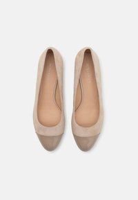 Ballerines en suède beige avec un bout caps lisse et brillant taupe. L'intérieur présente une doublure beige clair. Design épuré et épuré.