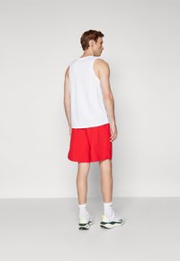 Weißes ärmelloses Tanktop und rote Shorts. Das Tanktop ist glatt, die Shorts sind leicht. Weiße Sportschuhe mit schwarzen und neon-grünen Akzenten.