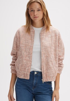 Veste bombardier texturée en rose doux avec fermeture éclair à l'avant, poignets côtelés et ourlet, assortie à un t-shirt à col rond blanc et un jean bleu.