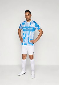 Μπλε και λευκή κοντομάνικη φανέλα ποδοσφαίρου με γεωμετρικά σχέδια και το κείμενο «CONCLUSION», συνδυασμένη με λευκά σορτς και κάλτσες.