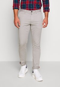 Pantalones de corte ajustado en gris claro con textura suave, acompañados de zapatillas blancas con un detalle en azul marino. Combinados con una camisa de cuadros roja y azul.