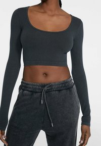 Dark green ribbed long-sleeve crop top with a wide scoop neckline, paired with gray drawstring sweatpants featuring a soft texture.