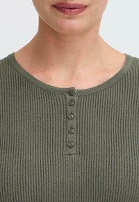 Olivgrön ribbad topp med rund halsringning, prydd med sju små knappar framtill och en mjuk, texturerad tyg.