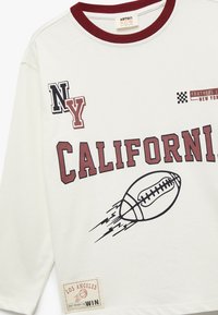 Weißes Langarmhemd mit weinroten Akzenten, bedruckte Grafiken einschließlich "CALIFORNIA", einem Fußball und Logos von NY und LA.