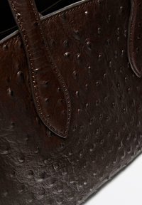 Borsa in pelle marrone scuro con texture di struzzo e manici cuciti, mostrata in dettaglio ravvicinato su sfondo bianco.