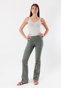 Pantaloni svasati verde scuro con una texture liscia e vita elastica, abbinati a una canotta grigia chiara e sandali marroni.