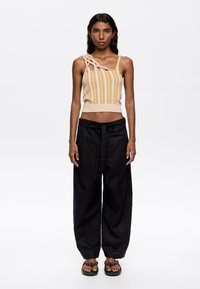 Knit tank top with vertical orange and cream stripes, one shoulder featuring a twisted detail. Loose black trousers with a tied waist.