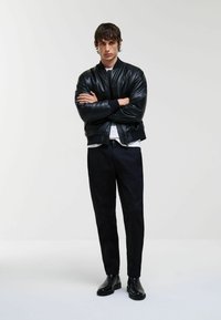 Jachetă bomber din piele neagră, cu manșete și tiv ribborat, combinată cu pantaloni skinny negri și bocanci negri până la gleznă. Finisaj neted și lucios.