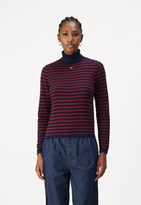 Maglione a collo alto blu navy con righe orizzontali rosse, dotato di un piccolo logo sul petto e realizzato in un materiale a maglia morbido e testurizzato.