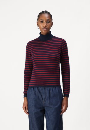 Mørkeblå turtleneck genser med røde horisontale striper, med en liten logo på brystet og mykt, strukturert strikket materiale.