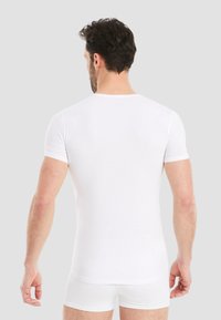 White short-sleeve t-shirt made of smooth cotton, fitted design, with a round neckline. Worn with matching white briefs, plain and seamless.
