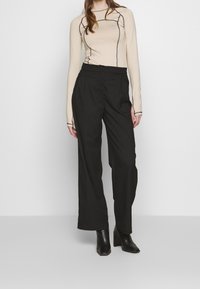 Beige langsl sleeve top met zwarte stikdetails, gecombineerd met hoge taille zwarte broeken en zwarte leren enkellaarsjes.