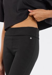 Czarne legginsy z wysokim stanem, wykonane z elastycznego materiału. Posiadają mały akcent logo z boku oraz gładką fakturę.