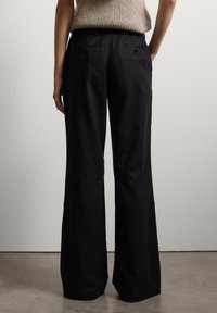 Zwarte wijde benen broek van een gladde stof met een subtiele textuur. Voorzien van twee achterzakken met knoopsluitingen.