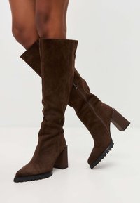 Stivali marroni al ginocchio in suede, con punta affusolata, tacco a blocco e cerniera laterale. Superficie testurizzata con suola rigata.
