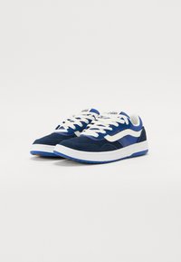 Navy blue sneakers made of suede and mesh, featuring white laces, a white side stripe, textured sole, and padded collar for comfort.