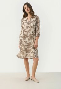 Helles beigefarbenes Kleid mit braunen Blattmustern, V-Ausschnitt, Dreiviertelärmeln und einem schwingenden Rock. Glattes Material mit einem fließenden Textur.