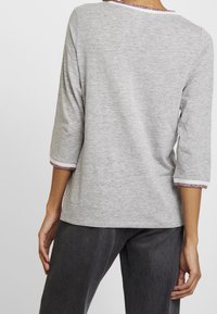 Helles graues Langarmshirt mit Rundhalsausschnitt und Dreiviertelärmeln, mit einem strukturierten pinken Saum an den Ärmeln. Weicher Stoff.
