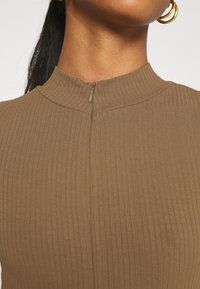 Top marrone a costine con colletto alto e una breve zip sul retro. Il tessuto ha una finitura liscia e testurizzata.